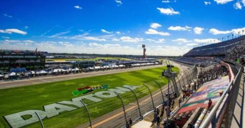 A panoramic view of Daytona International Speedway, featuring a clear blue sky and a bustling crowd.