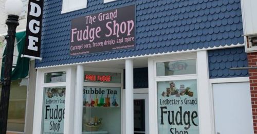 Exterior of The Grand Fudge Shop featuring a blue shingle facade and signs for fudge, bubble tea, and free fudge.