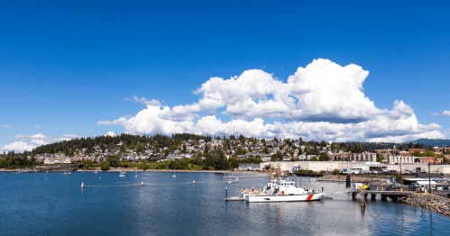 A scenic view of a harbor with a boat, surrounded by hills and a blue sky filled with fluffy clouds.