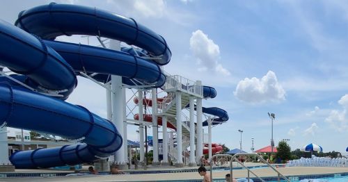 A water park featuring blue water slides, a swimming pool, and people enjoying the sunny day.