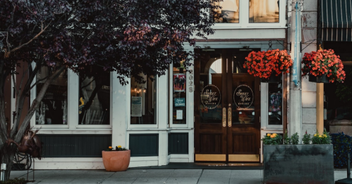 A charming storefront with wooden doors, large windows, and vibrant flower baskets hanging outside.