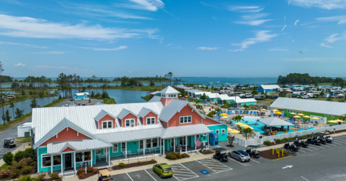 A colorful waterfront resort with a pool, surrounded by greenery and water, under a clear blue sky.