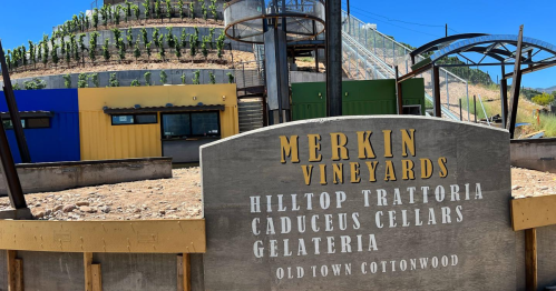Sign for Merkin Vineyards with a hillside vineyard and modern building in the background under a clear blue sky.