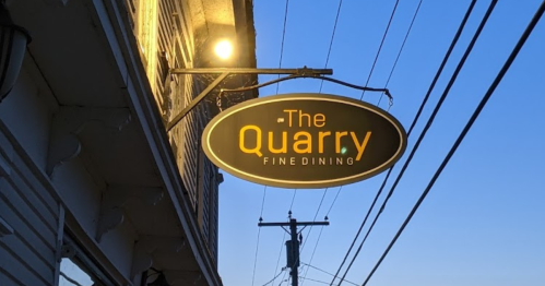 Sign for "The Quarry Fine Dining" illuminated against a twilight sky, with power lines in the background.