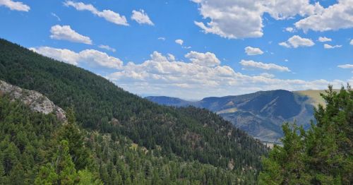 Lush green mountains under a bright blue sky with fluffy white clouds, showcasing a serene natural landscape.