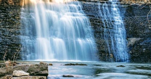 A serene waterfall cascading over rocky cliffs into a calm pool below, surrounded by nature.