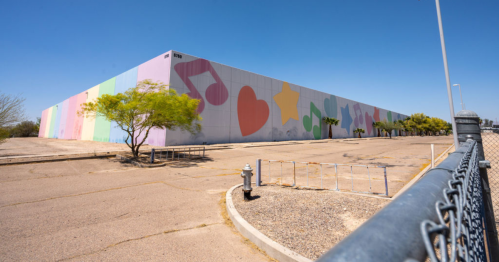 Colorful mural on a large building wall, featuring musical notes and shapes, with a clear blue sky above.