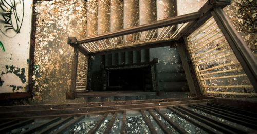Aerial view of a worn staircase with peeling paint and debris, leading down into darkness.