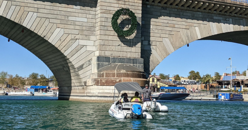 Two boats are moored near a bridge decorated with a large wreath, under a clear blue sky.