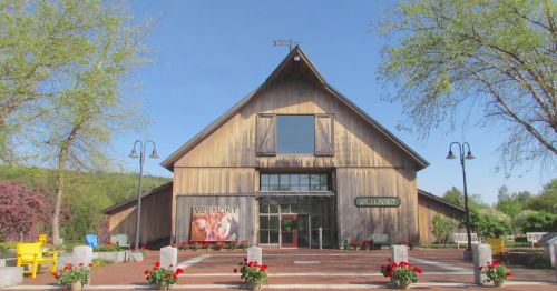 A large wooden barn-style building with a sign, surrounded by flowers and trees under a clear blue sky.