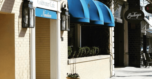 A sunny street scene featuring a café with blue awnings and a nearby restaurant sign.