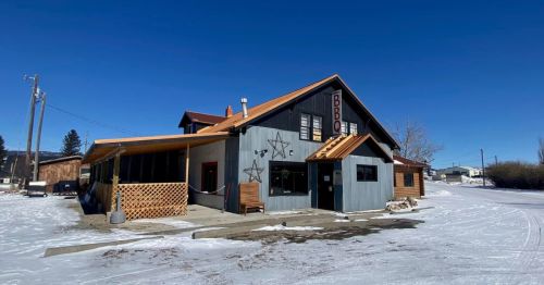 A rustic building with a sloped roof, wooden accents, and a star design, surrounded by snow under a clear blue sky.