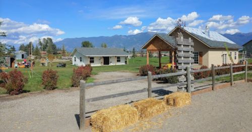 A scenic farm with buildings, hay bales, and mountains in the background under a clear blue sky.
