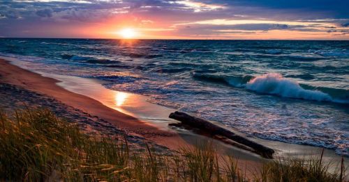 A serene beach at sunset, with gentle waves, a sandy shore, and a colorful sky reflecting on the water.