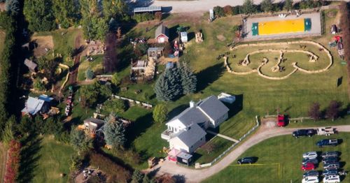 Aerial view of a large property with a house, gardens, and a unique maze design in the lawn, surrounded by trees.