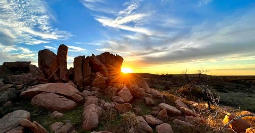 Sunset over rocky terrain, with vibrant colors and sun rays shining through the clouds in a serene landscape.