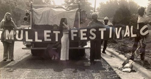 A group of people holding a large banner that reads "Mullet Festival" in front of a truck.