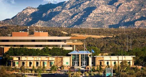 A modern building with flags in front, set against a backdrop of mountains and clear blue sky.
