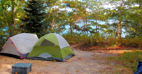 Two tents set up at a campsite near a lake, surrounded by trees and autumn foliage.