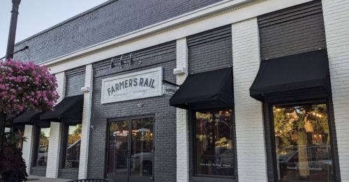 Exterior of a building with a sign reading "Farmer's Rail," featuring large windows and black awnings.