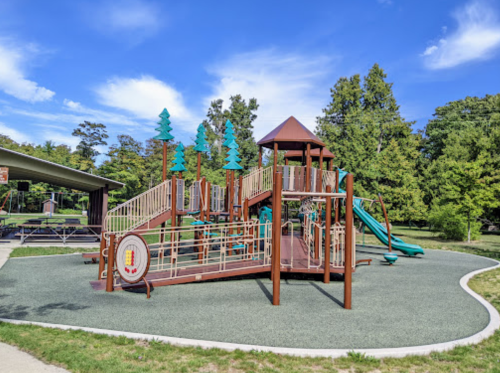A colorful playground with slides and climbing structures, surrounded by green trees and a clear blue sky.