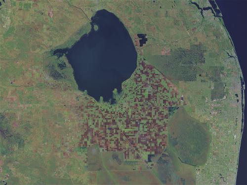 Aerial view of a large, green agricultural area with a dark lake in the center and patchwork fields surrounding it.