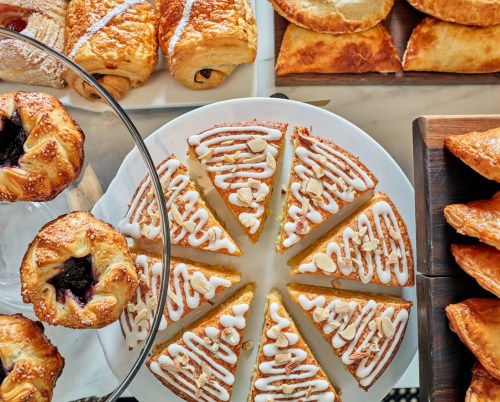 A variety of pastries, including croissants and iced cake slices, arranged on platters.