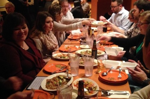 A group of people enjoying a meal at a restaurant, sharing dishes and drinks around a long table.