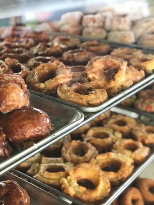 A display of various donuts and pastries on trays, including glazed and ring-shaped options.