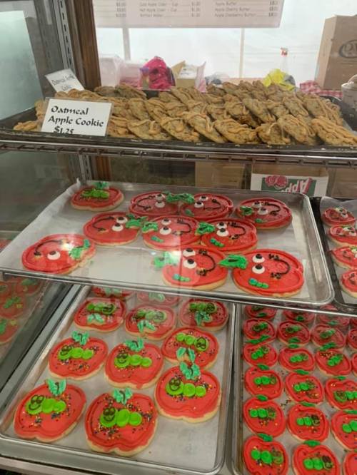 A display case filled with decorated cookies, including red apple-shaped cookies with green leaves and oatmeal cookies.