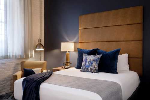 Cozy bedroom featuring a large bed with blue pillows, a stylish lamp, and a comfortable armchair.