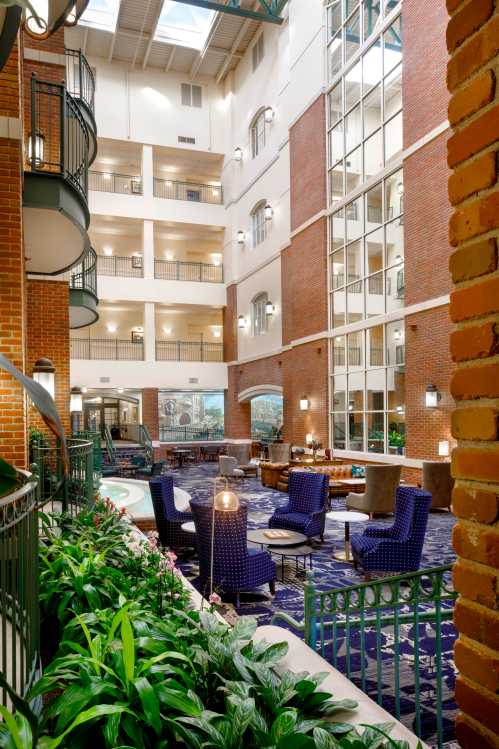 Interior view of a hotel atrium featuring plants, seating areas, and large windows, creating a bright and inviting atmosphere.