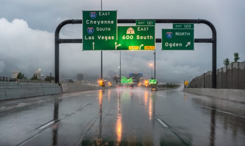 Highway signs indicating directions to Cheyenne, Las Vegas, and Ogden, with wet pavement and overcast skies.
