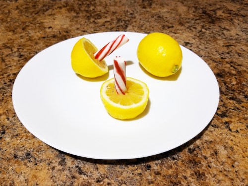 A white plate with two whole lemons and one lemon half, topped with red and white striped candy canes.
