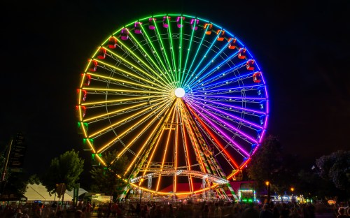 A brightly lit Ferris wheel at night, illuminated in vibrant rainbow colors against a dark sky.
