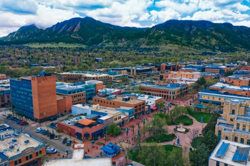 Aerial view of a vibrant downtown area with shops, people, and mountains in the background under a partly cloudy sky.
