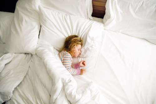 A young child peacefully sleeping in a bed surrounded by white pillows and blankets.