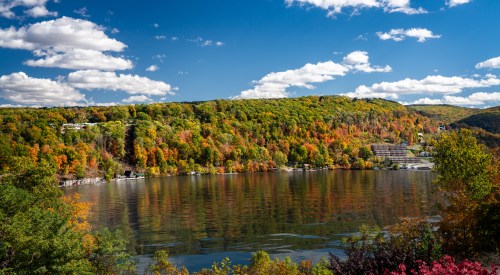 A serene lake surrounded by vibrant autumn foliage and a clear blue sky with fluffy clouds.
