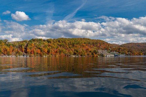 A serene lake scene reflecting colorful autumn foliage and a cloudy blue sky.