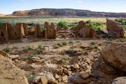 Ruins of an ancient structure surrounded by rocky terrain and sparse vegetation under a clear blue sky.