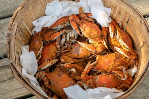 A wooden basket filled with cooked crabs, seasoned and resting on white paper towels.