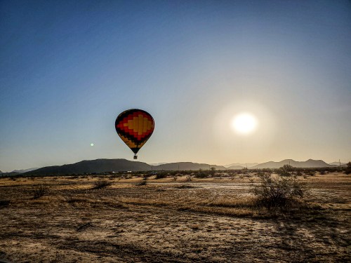 A colorful hot air balloon floats over a desert landscape at sunrise, with mountains in the background.