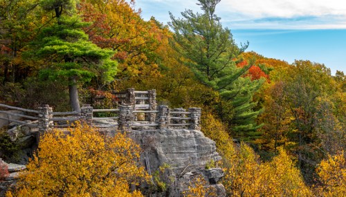Scenic view of a rocky overlook surrounded by vibrant autumn foliage and clear blue skies.