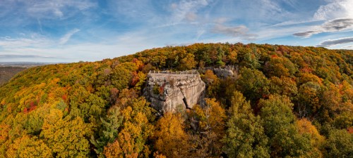 A panoramic view of a rocky outcrop surrounded by vibrant autumn foliage in a scenic landscape.