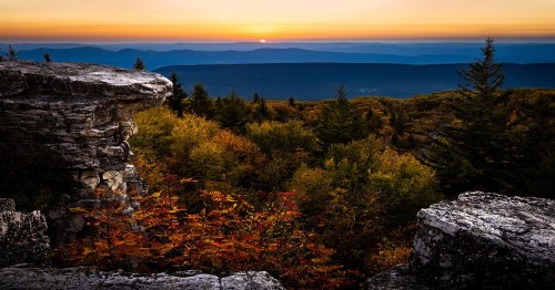 Sunset over a mountainous landscape, with vibrant autumn foliage and rocky outcrops in the foreground.