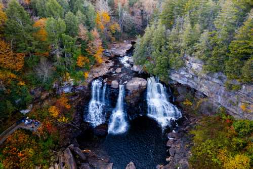 Aerial view of a waterfall surrounded by colorful autumn foliage and rocky terrain.