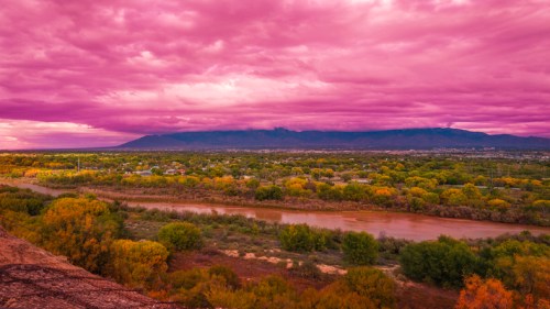 A vibrant pink sky over a lush landscape with a winding river and distant mountains.