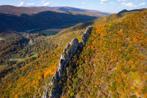 Aerial view of a rocky ridge surrounded by vibrant autumn foliage and rolling hills under a clear blue sky.