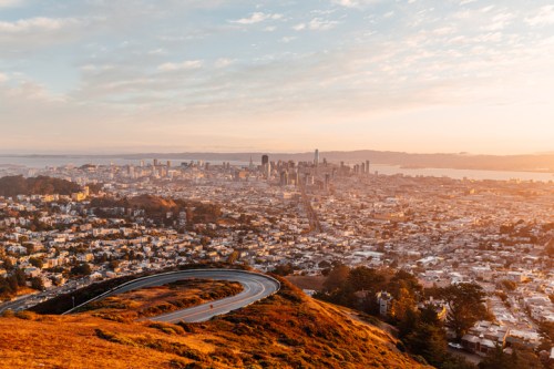 A panoramic view of San Francisco at sunset, showcasing the skyline and winding road on a hillside.