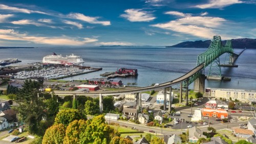 Aerial view of a bridge over water, with a cruise ship docked nearby and a scenic landscape in the background.
